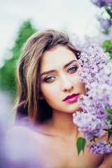 Naklejka premium Portrait of young beautiful woman posing among lilac trees.