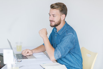 Fototapeta premium Young smiling businessman working in his office and typing on his laptop.