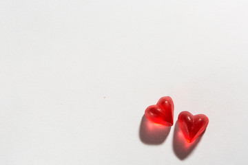 illuminated small hearts with shadows on white background; heart-shaped jelly candy like pieces of glass