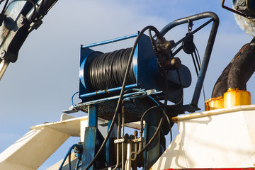A large cable reel with pulley wheel on the deck of a small fishing trawler