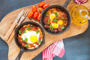 Pan of fried eggs and cherry-tomatoes with bread on dark table surface, top view, copy space, selective focus