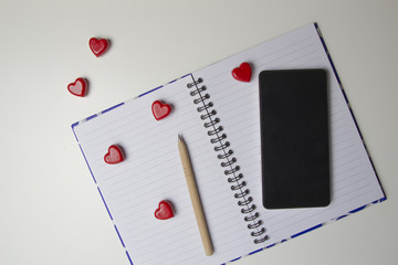 Open notebook with red hearts and mobile phone on it. White background. Top view