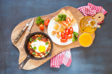 Pan of fried eggs and cherry-tomatoes with bread on dark table surface, top view, copy space, selective focus