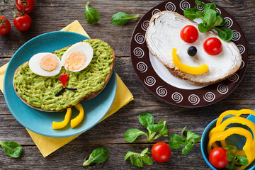Funny colorful creative meal idea for kids: avocado sandwich with hard boiled egg, pepper nose and black olive mustage; cream cheese sandwich with vegetable face and corn salad 