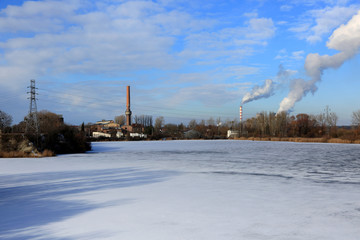 Krajobraz zimowy, dymiące kominy elektrowni, cegielnia i słupy elektryczne.