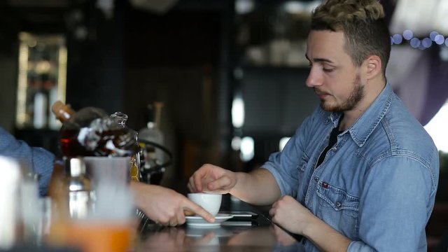A young man uses tablet and drink coffee while sitting at the bar