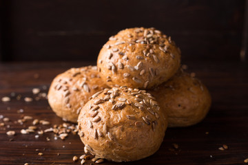 Four buns with seeds on a dark wooden background, top view