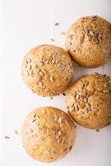 Four buns with seeds on a light wooden background, top view