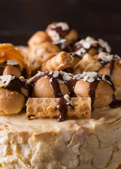 Napoleon cake on a dark wooden background decorated with petals of almonds eclairs, waffles and chocolate icing