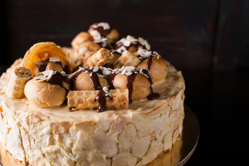 Napoleon cake on a dark wooden background decorated with petals of almonds eclairs, waffles and chocolate icing