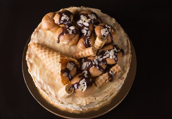 Napoleon cake on a dark wooden background decorated with petals of almonds eclairs, waffles and chocolate icing