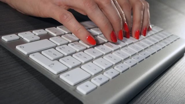 Woman with long fingers and red nails typing on a wireless computer keyboard, close up view