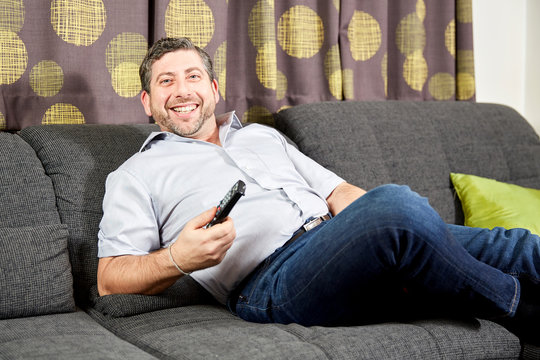 Man watching TV on sofa at home smiling