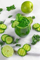 Fresh Green smoothie with kale, cucumber, lime, apple, parsley on white board.