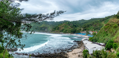 Panorama photo of shore or beach with houses and traditional boat for fisherman in faraway, with waves broken forming white foam, captured from top. Captured on Menganti Beach, Kebumen, Indonesia
