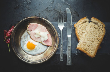 Top view of the fried egg with chili peppers, ham and toasted bread on a dark background ... ...