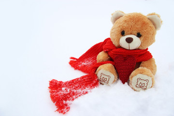 Игрушечный мишка на снегу с вязанным сердцем