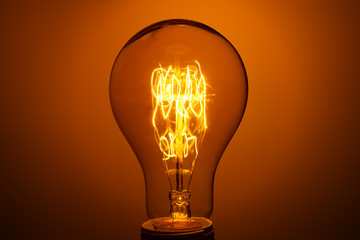 lighted vintage incandescent bulb on orange background