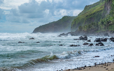 Photo of beautiful beach in cloudy day, when big wave hit the beach. And with beautiful green cliff in the back. Captured on Menganti Beach, Kebumen, Indonesia