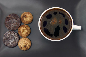 cup of black coffee with biscuits on a dark plate