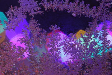 Frost ice crystals on window with colored lights at night seasonal wintery