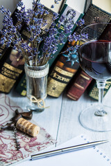 Glass of red wine, a bouquet of lavender, open notepad, pen and a book on a white wooden background