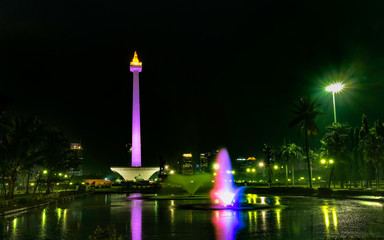 National Monument (Monas) at night, in front of big pool and colorful water fountain, create beautiful reflection of this monument., this is one of iconic monument in Jakarta, Indonesia
