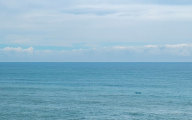 Obraz premium Small boat in almost empty sea, with beautiful cloudy sky, separated with sea by the horizon.
