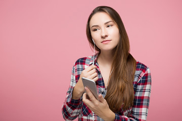 hipster girl enjoying listening to the phone playlist in headphones over pink background isolated
