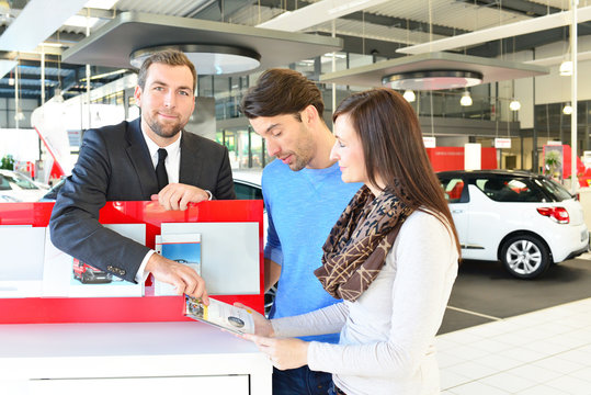 Verkauf von Fahrzeugen im Autohaus: Verkäufer berät junges Paar