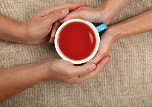 Man and woman hands holding full black tea cup