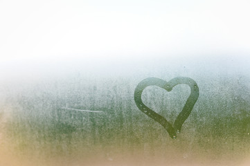 Abstract blurred love heart symbol drawn by hand on the wet frozen window glass with sunlight background. - obrazy, fototapety, plakaty