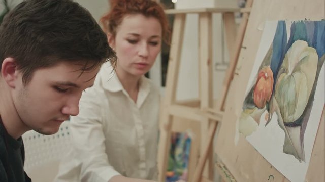 Female artist teaching young male student to paint with watercolor