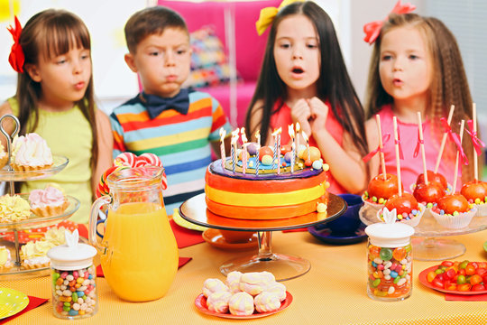 Children blowing candles on tasty cake at birthday party