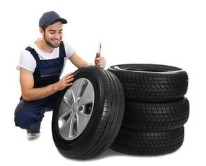 Fototapeta premium Young mechanic in uniform with wheels on white background