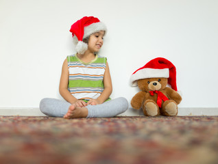 Little kid in Santa hat with cute teddy bear waiting at home for