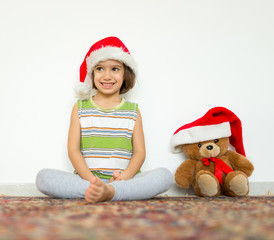 Little kid in Santa hat with cute teddy bear waiting at home for