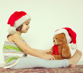 Little kid in Santa hat with cute teddy bear waiting at home for