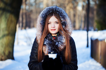 Fototapeta na wymiar Young and attractive woman on walk, winter, warm coat with a hood, coffee to go