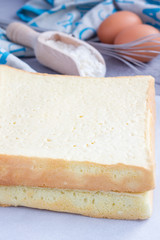 Two layers of homemade freshly baked square sponge cake, ingredients on background, vertical