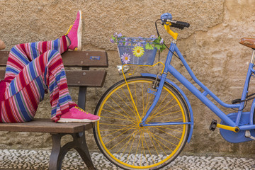 Farbenfrohe Frauenbeine rasten auf einer Bank neben buntem Fahrrad