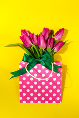 Fresh beautiful lila tulips in gift package on bright yellow bac