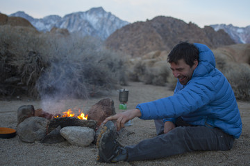 An adult man stretching and keeping warm by his campfire in the Alabama Hills.  Lone Pine, California.