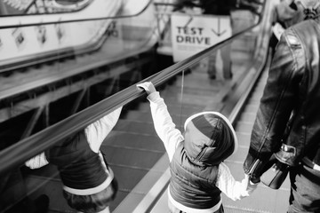 Black and white image back view of mother and child going together on escalator background. Shopping mall, airport travel, love care