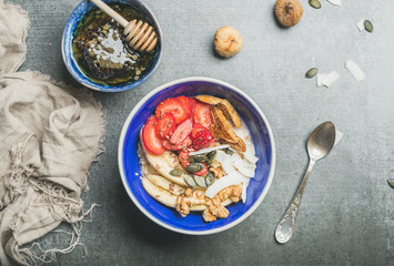 Yogurt, granola, seeds, fresh and dry fruits and honey in blue ceramic bowl over grey concrete background, top view, horizontal composition. Clean eating, detox, dieting, vegetarian food concept