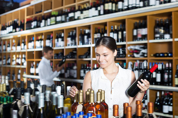 Young woman choosing bottle in wine shop