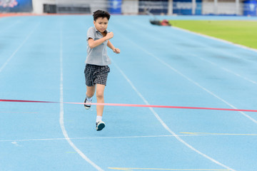 Fototapeta na wymiar Young Asian boy running on blue track in the stadium