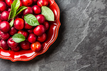 Fresh plums with leaves on red plate. Slate background