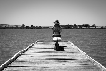 Woman sitting on pier looking out over the water - 133356330