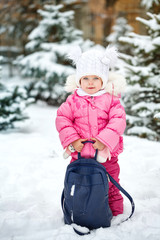 Fototapeta na wymiar Pretty little girl in winter park. She holds a big backpack. Outdoor Activities. Close-up portrait